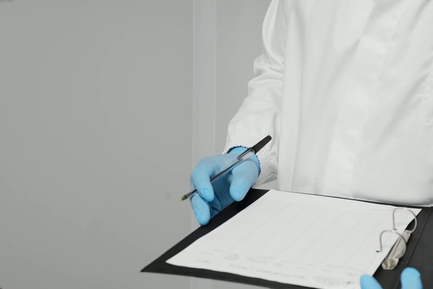 A gloved hand signing a batch record on a clipboard