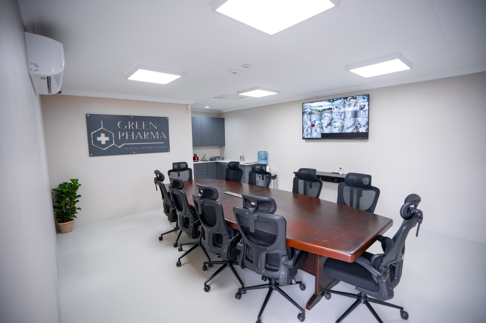 The on-site boardroom, a long table and ten chairs beneath the Green Pharma wall sign, with a CCTV wall monitor at the far end