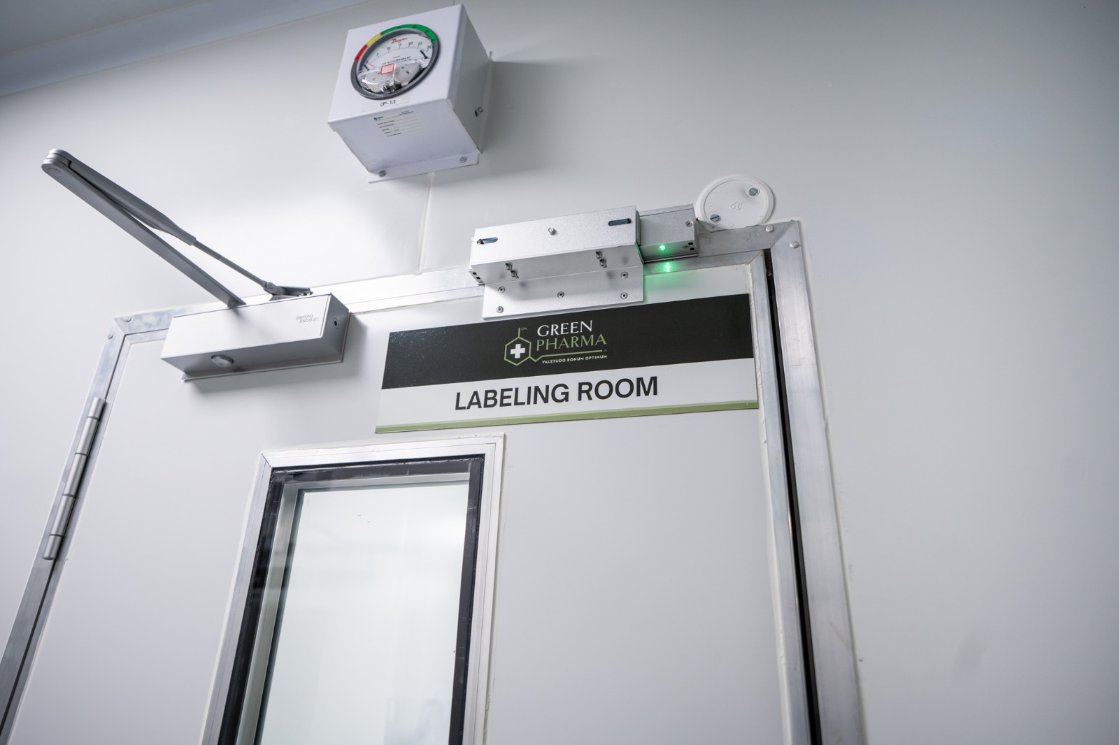 The door to the labelling room, its sign lit from the side, with a differential pressure gauge mounted above it and a magnetic lock showing green