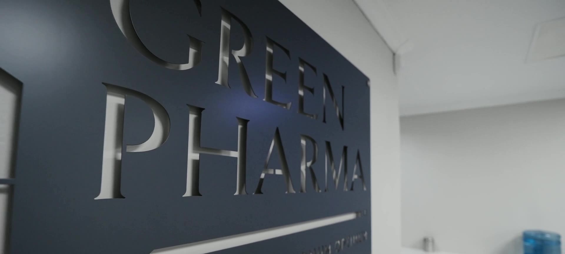 The Green Pharma wordmark in raised metal letters on a dark wall in reception