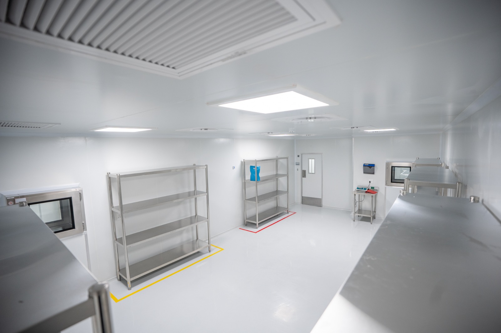 A staging room with empty stainless racking, ceiling air diffusers overhead and pass-through hatches set into the walls at both ends